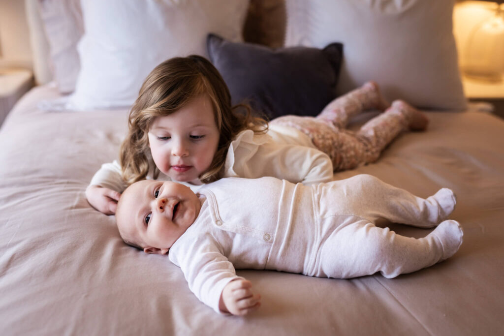 Baby boy lying beside older sister on bed during relaxed family newborn session