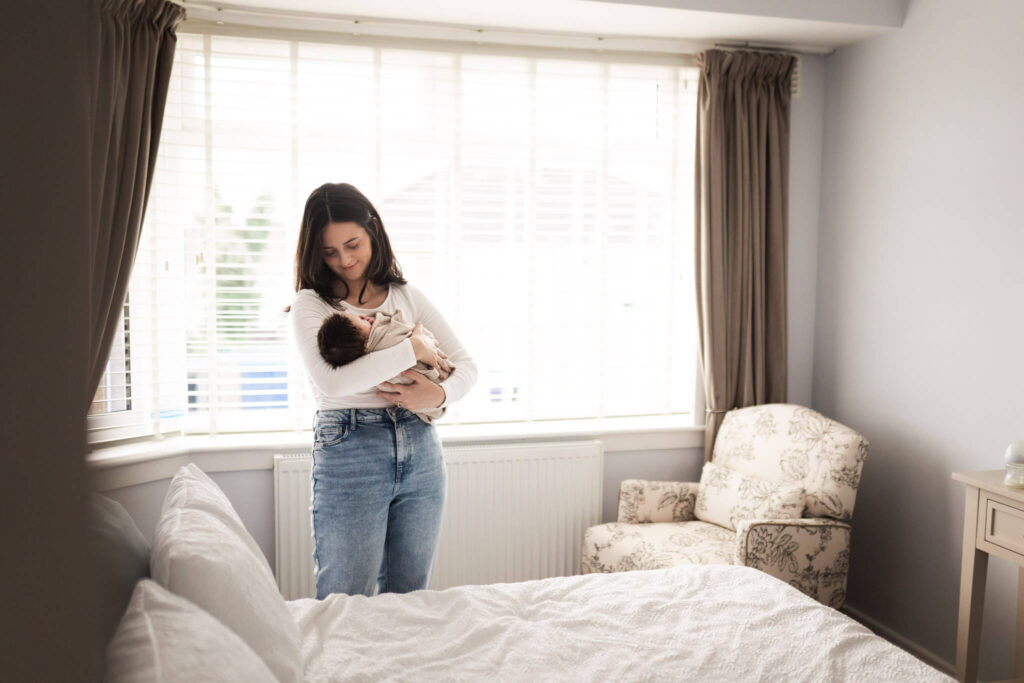 Mother standing in the bedroom holding her newborn baby during an at-home newborn photoshoot in Glasgow