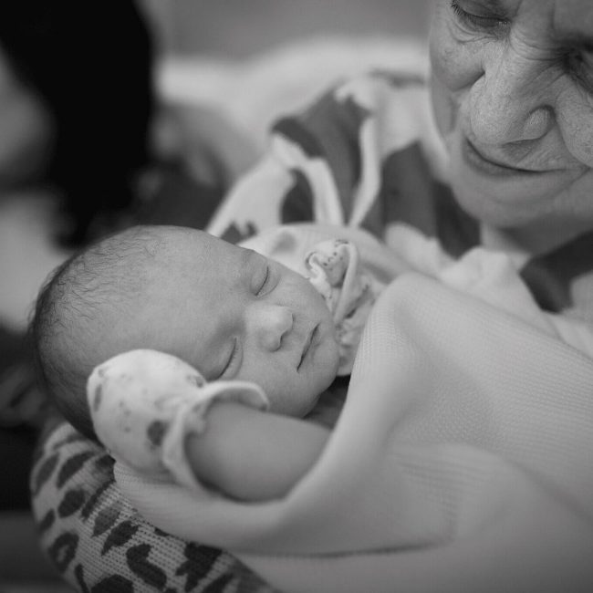 grandmother holding in arms new born baby boy, in hospital photoshoot