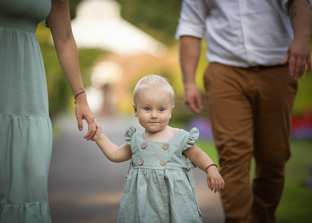 one year old girl in green linen dress walking with parents in the park, family lifestyle photoshoot