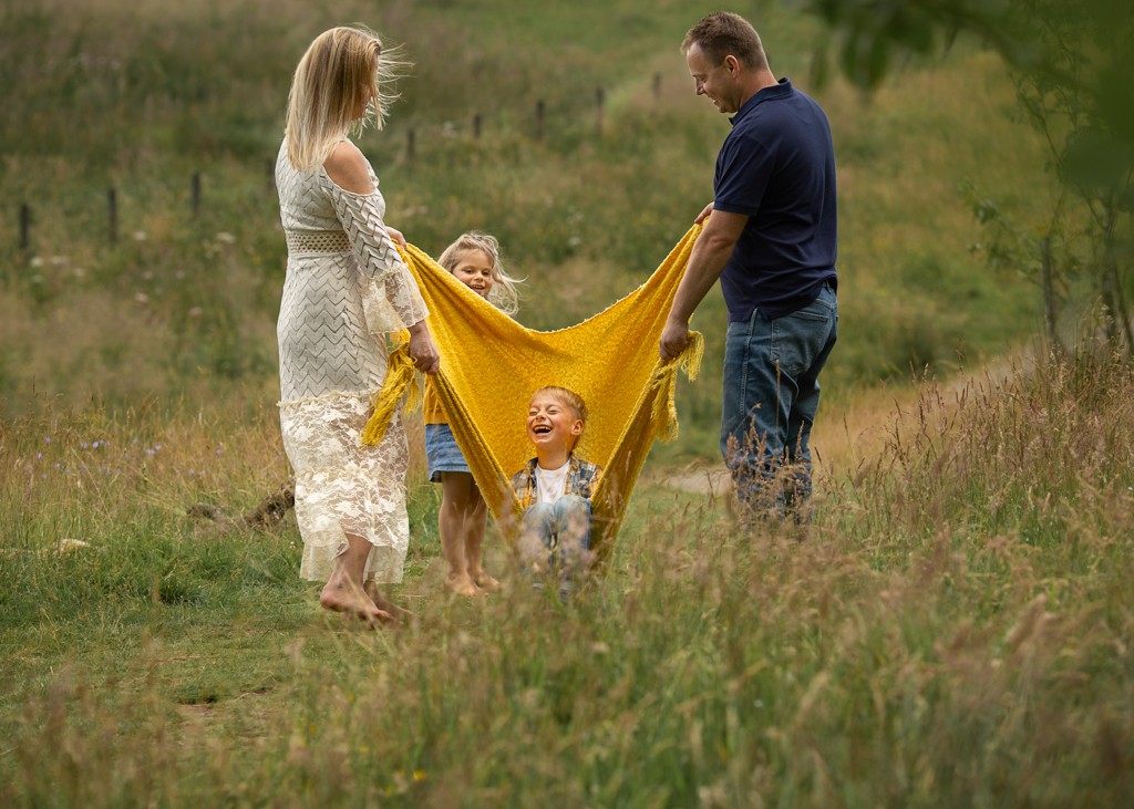 family of four with two pre school children playing with a blanket swing in the park, summer family lifestyle photoshoot