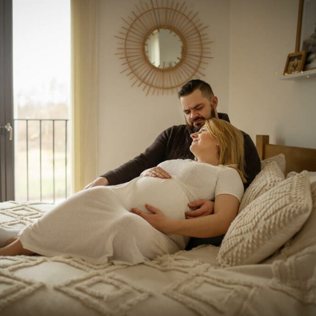 pregnancy couple cuddling on the bed in the bedroom, maternity in home lifestyle photoshoot