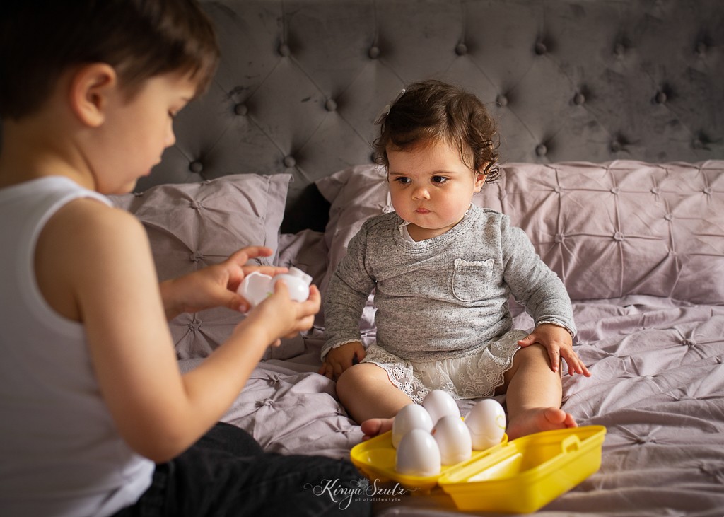 brother and one year old sister playing eggs toy on the bed, family photoshoot at the home