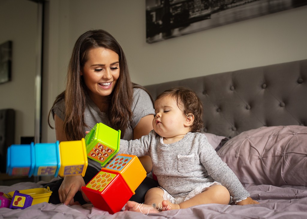 mom and one year old daughter building baby tower toy on the bed, relaxed photoshoot at the home