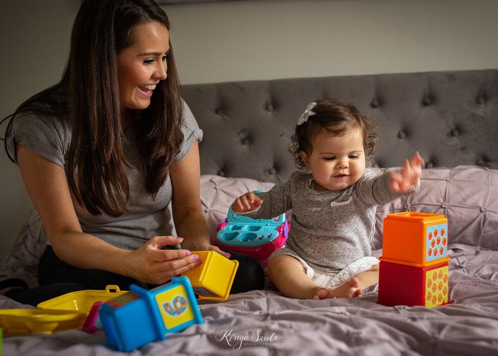 mom and one year old daughter building baby tower toy on the bed, relaxed family photoshoot at the home