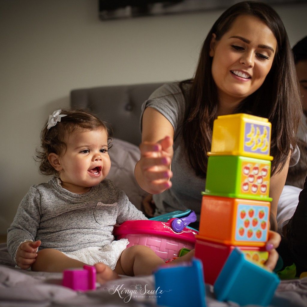 mom and one year old daughter building baby tower toy on the bed, relaxed photoshoot at the home