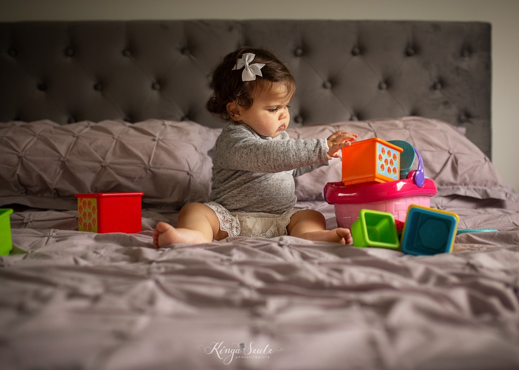 on year old baby girl sitting on the bed and paying toys, family photoshoot at home