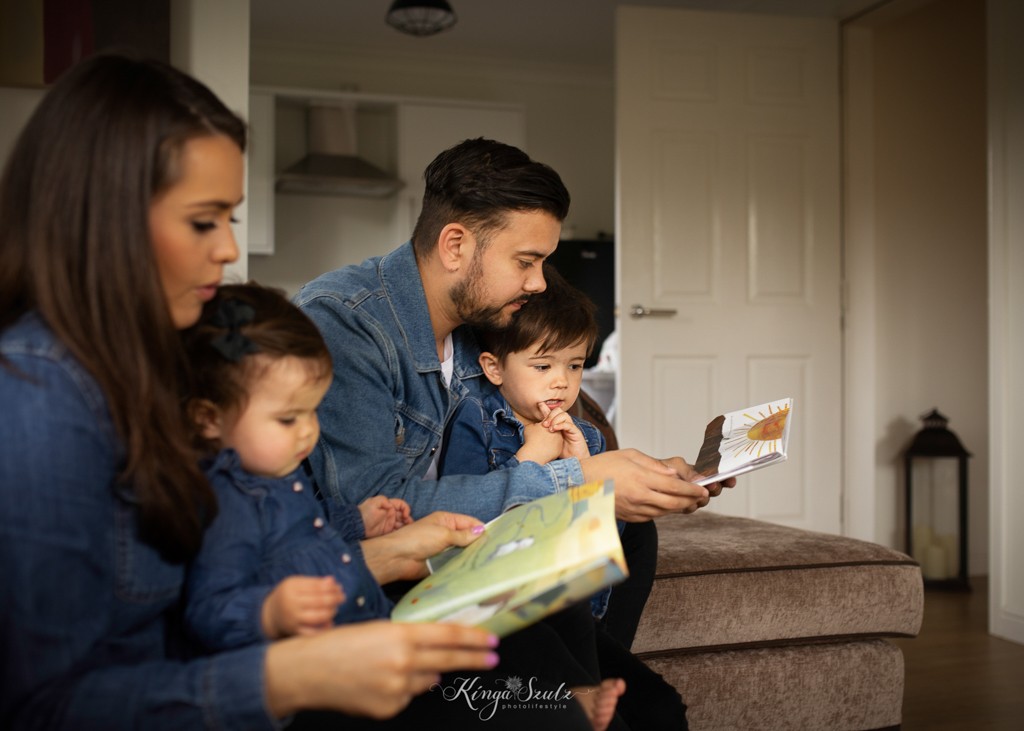 family of four sitting on the coach in the livingroom, reading baby books, family photoshoot in the home