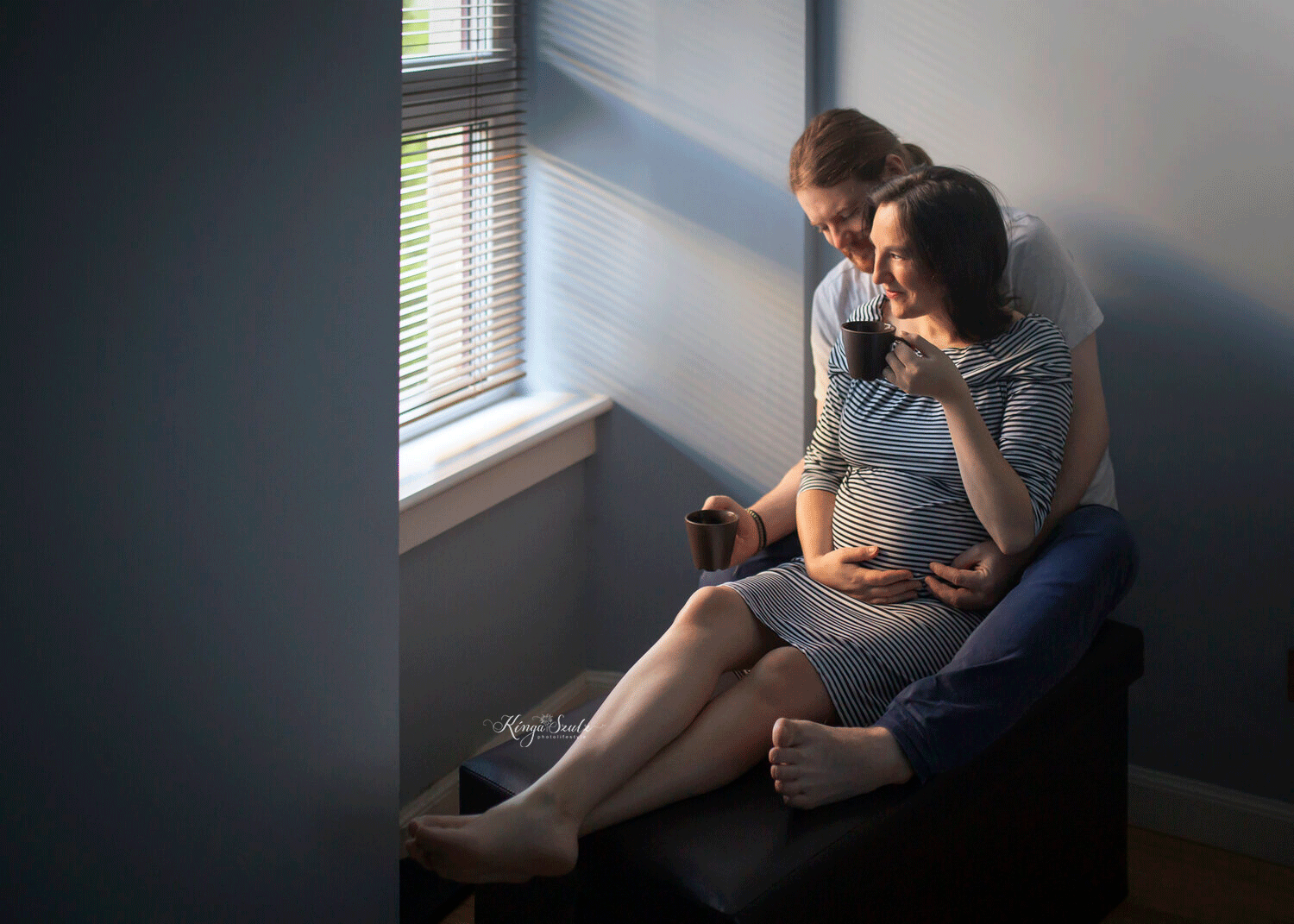 pregnancy couple with brown mugs, sitting next to the window, in home maternity photoshoot