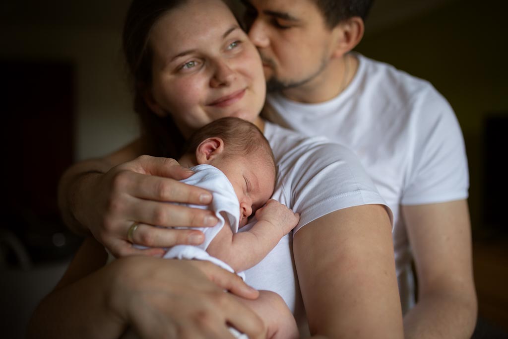 Parents cuddling their sleeping newborn baby together during an at-home newborn photoshoot in Glasgow