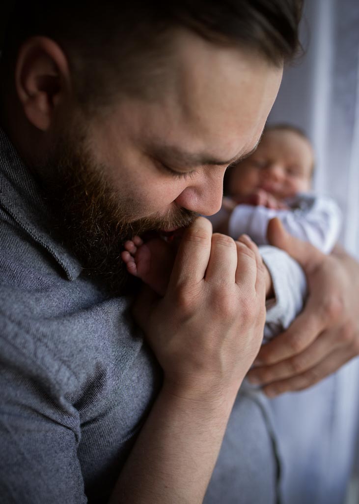 Dad gently kissing his newborn baby's tiny feet with the baby softly blurred in the background