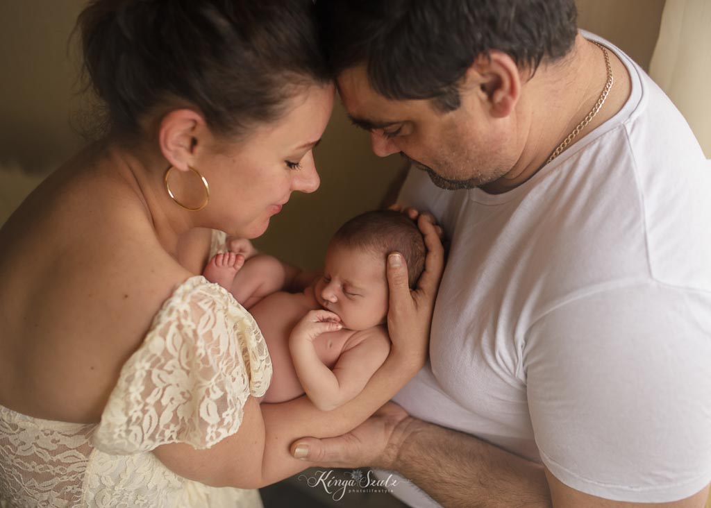 Parents gently holding and looking at their newborn baby during a natural lifestyle newborn photoshoot in Glasgow