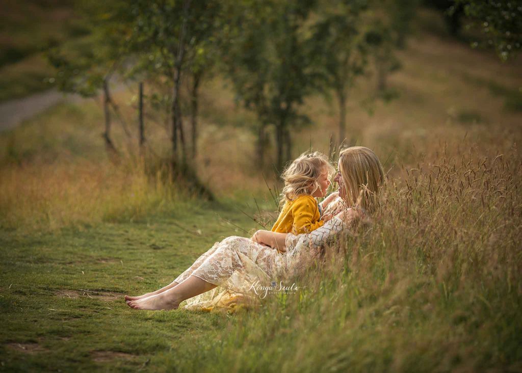 Mother and daughter laughing and cuddling together on a meadow during an outdoor family photoshoot in Glasgow