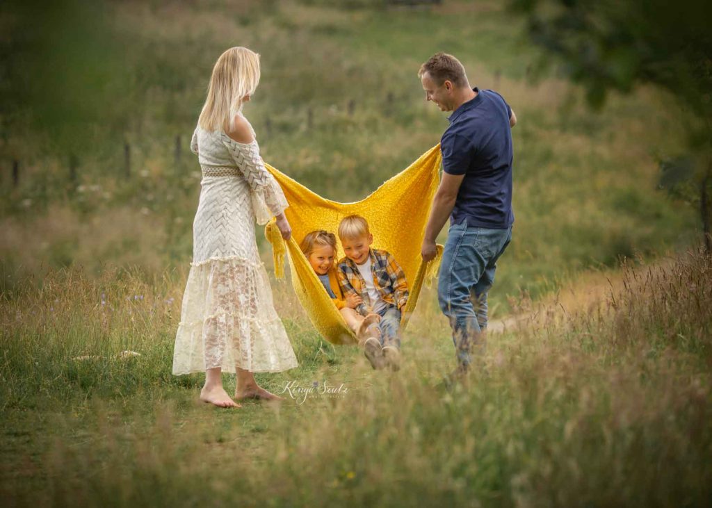 parents playing with a yellow blanket in a meadow during an outdoor family photoshoot