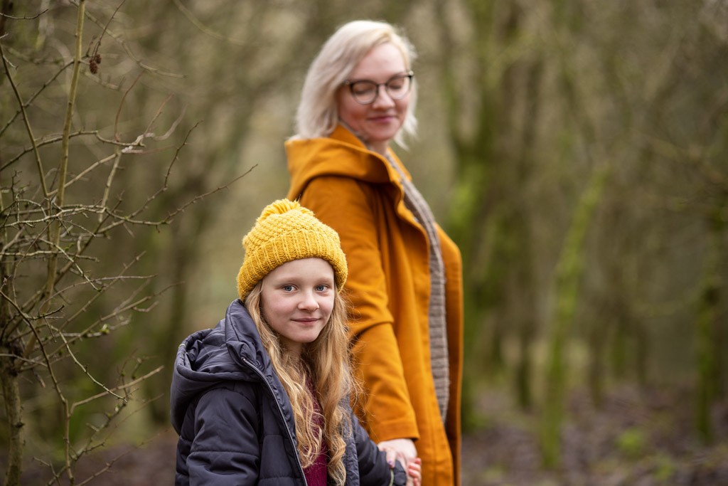Mother and daughter holding hands and looking at the camera during a winter family photoshoot in Glasgow, wearing a yellow coat and matching yellow hat