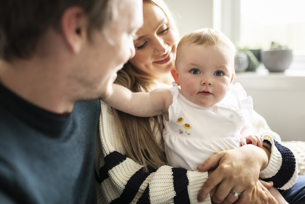 Parents holding their awake newborn baby as the baby looks towards the camera during an at-home newborn photoshoot in Glasgow