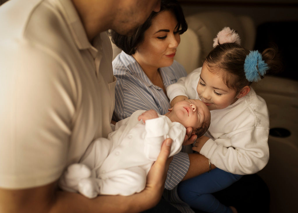 Parents cuddling their newborn baby on the bed as their older daughter leans in close during an at-home family newborn photoshoot in Glasgow