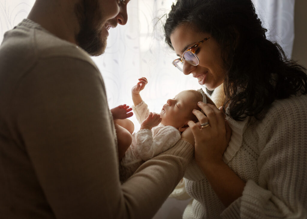 Parents cuddling their newborn baby together on the bed during a relaxed lifestyle newborn photoshoot in Glasgow