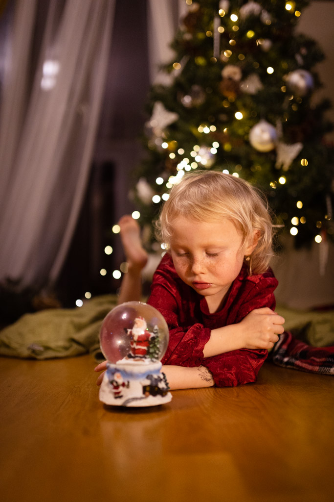 girl with a snow globe lay on the floor with a Christmas tree at the background