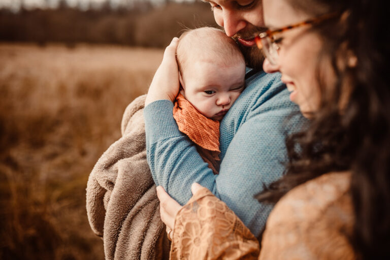 Parents cuddling their newborn baby in a blanket during an outdoor newborn photoshoot in Glasgow