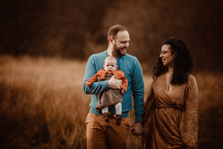 Parents walking with their newborn baby through a meadow during an autumn outdoor newborn photoshoot in Glasgow