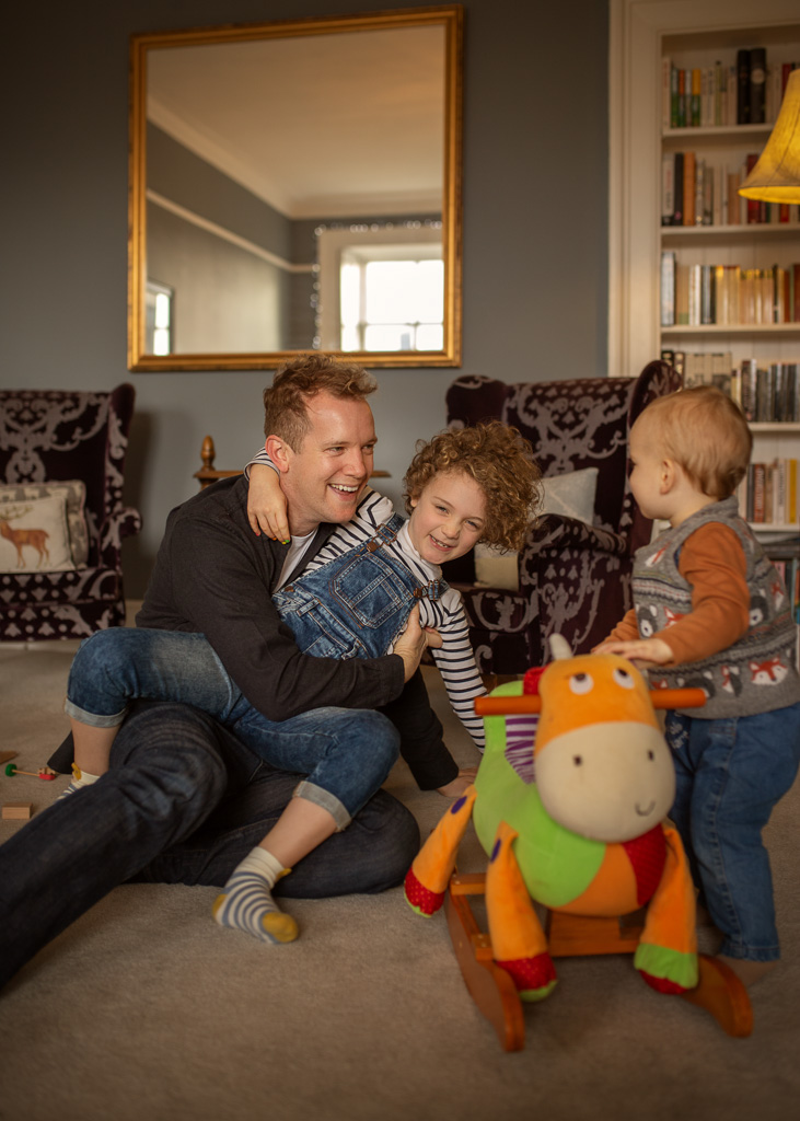 smiling kids, girl and boy, lying on the carpet among wooden blocks and goof with their dad, during a family photoshoot