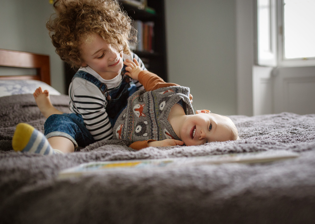 smiling sister and brother goofing on the bed during a family photoshoot at home