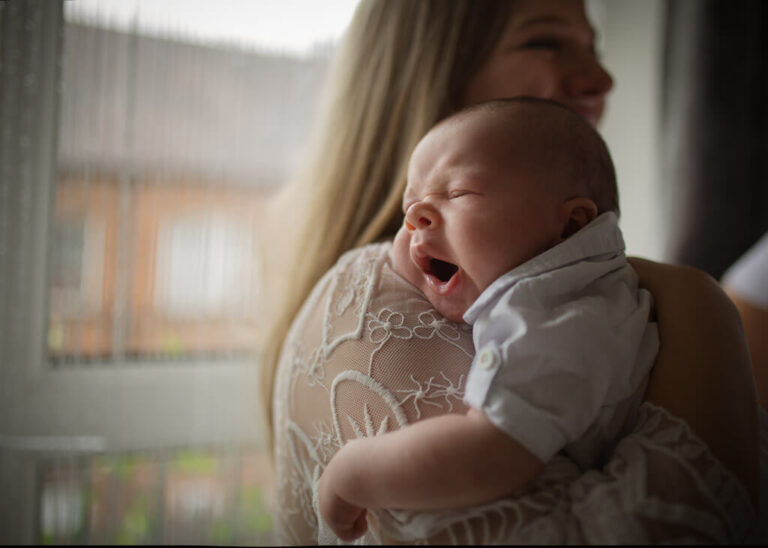 Mother holding her yawning newborn baby beside a window during an at-home newborn photoshoot in Glasgow