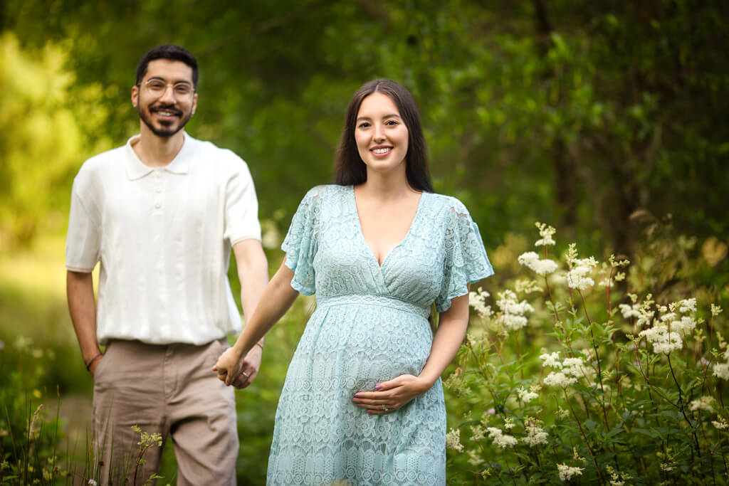 Couple holding hands and smiling at the camera during a summer maternity photoshoot in Glasgow
