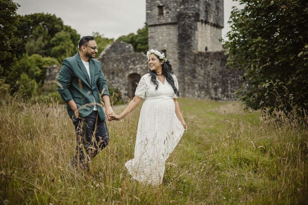 Expectant couple holding hands beside a castle ruin during an outdoor maternity photoshoot in Scotland