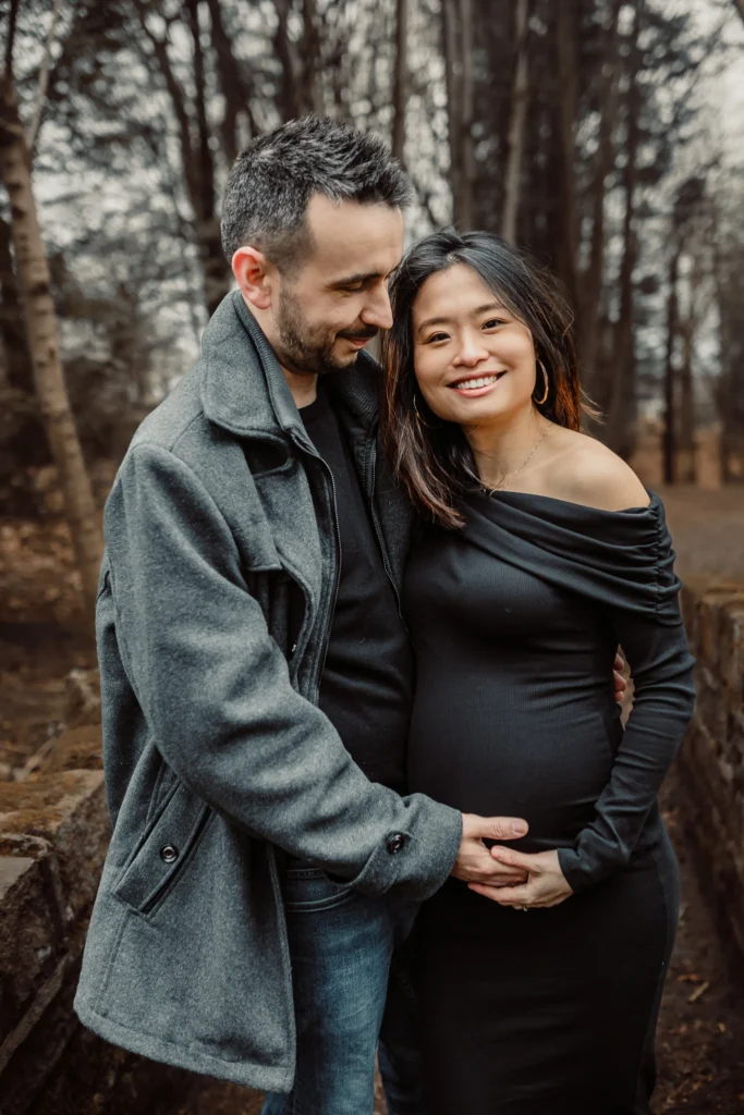Smiling expectant couple holding the bump together in autumn woodland during a maternity photoshoot near Glasgow