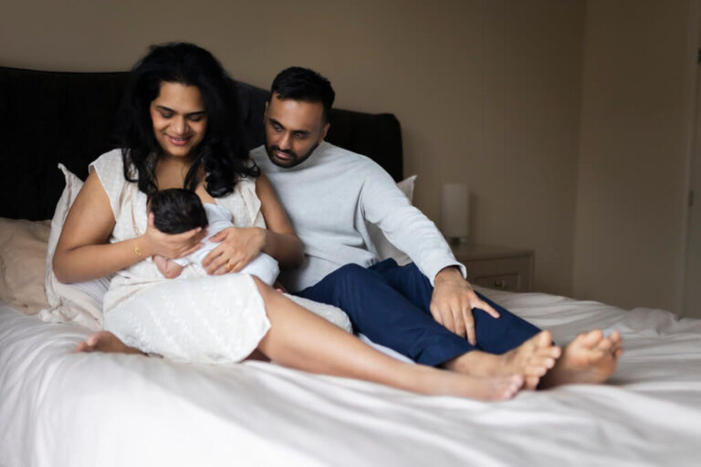 Parents sitting together on their bed and looking at their newborn baby during an at-home newborn photoshoot in Glasgow