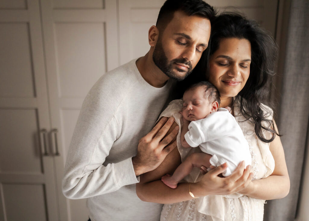 Mum, dad and newborn baby girl cuddling together during an at-home newborn photoshoot in Glasgow