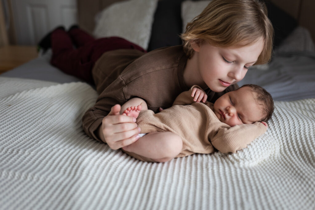 Older sibling lying beside their sleeping newborn sibling during a family newborn photoshoot in Glasgow