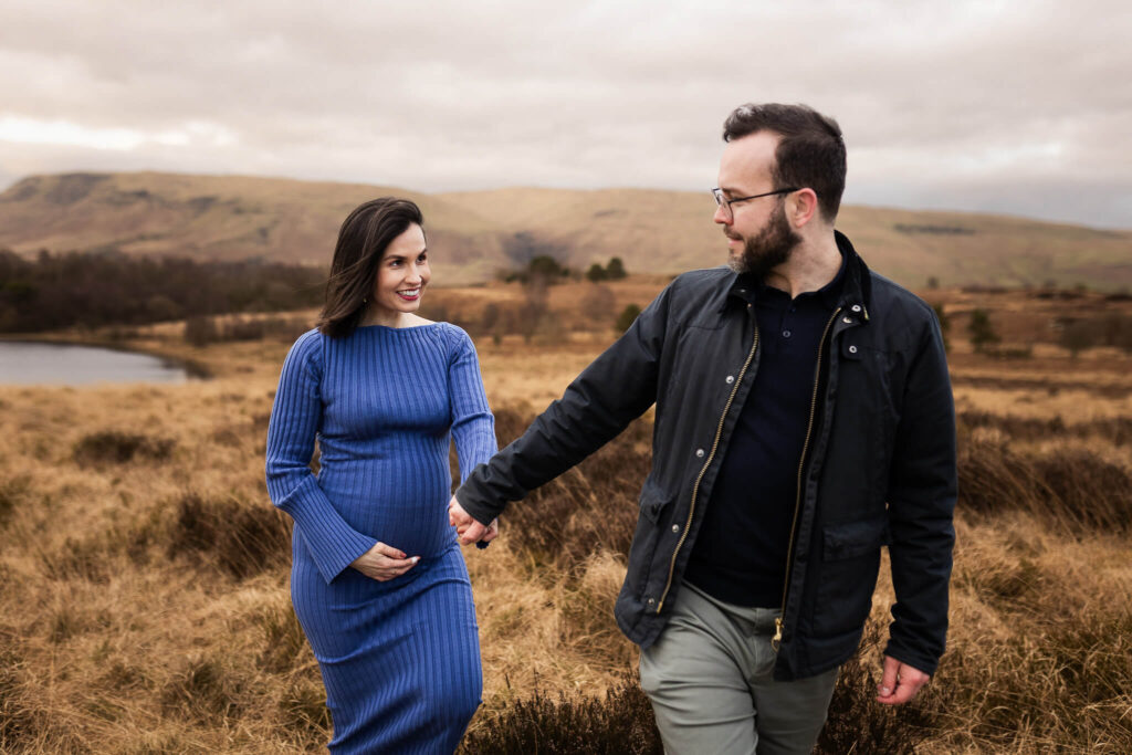 Couple holding hands and looking into each other’s eyes during a maternity photoshoot on a meadow near Glasgow