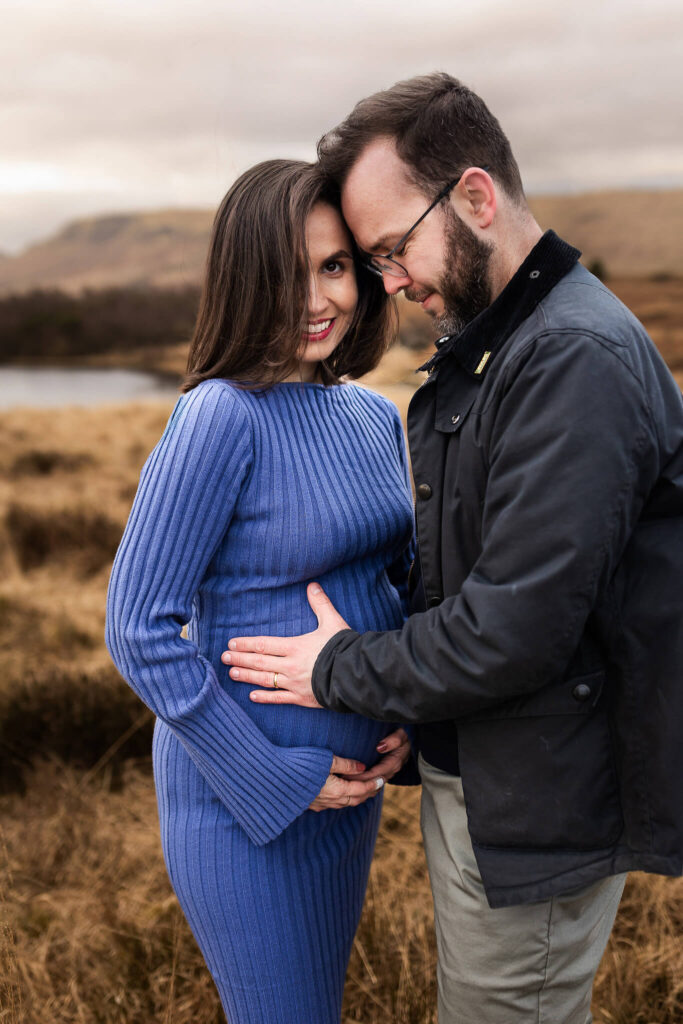Pregnant woman smiling at the camera as her partner holds her bump during a maternity photoshoot in Glasgow