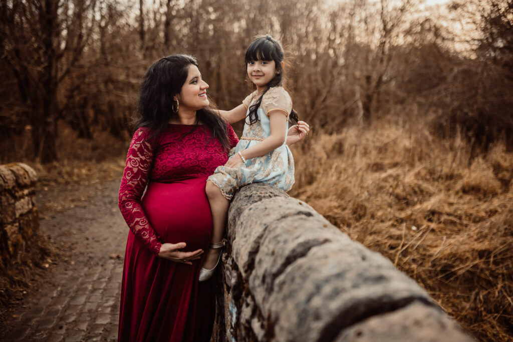 Pregnant woman looking at her daughter sitting on a wall during an outdoor maternity photoshoot in Glasgow