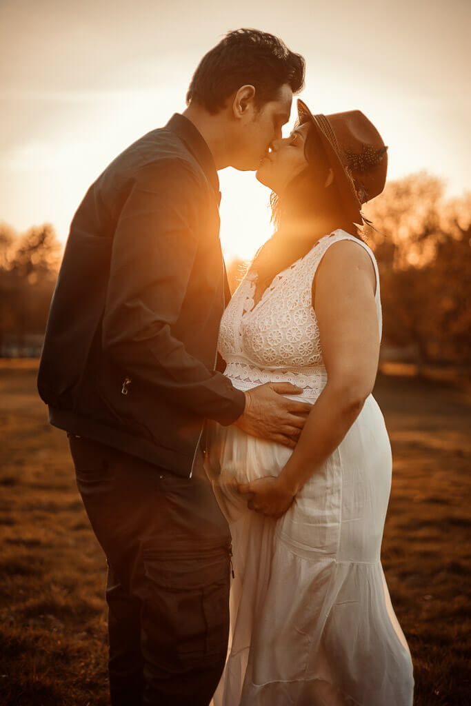 Couple embracing and kissing at sunset during a maternity photoshoot in Glasgow, with the sun shining through them
