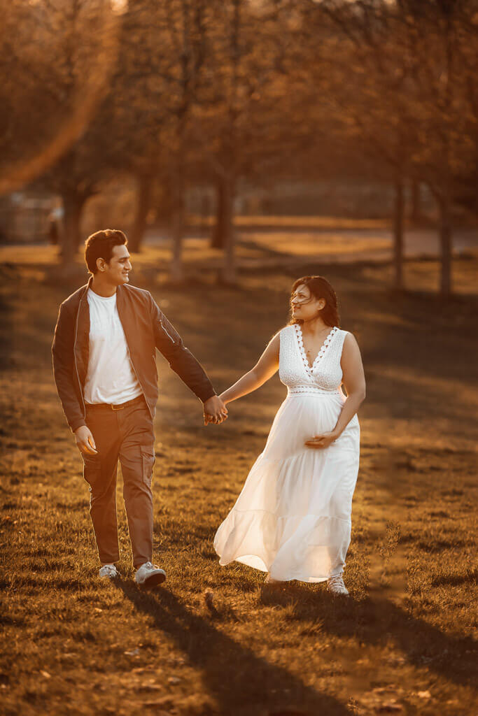 Pregnant woman and her partner walking hand in hand and looking at each other during a sunset maternity photoshoot in Glasgow