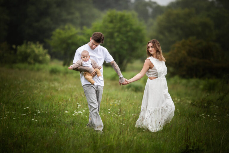 Family with a young child posing on a meadow during a summer outdoor photoshoot in Glasgow, wearing coordinated white outfits
