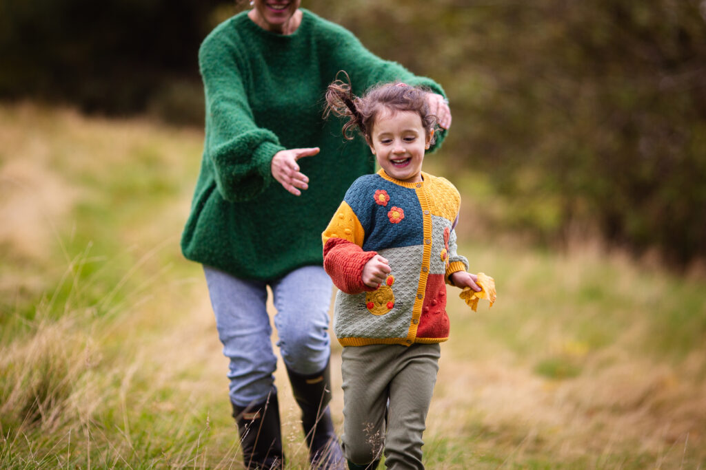 Mother chasing her daughter as they laugh together during an outdoor family photoshoot in Glasgow