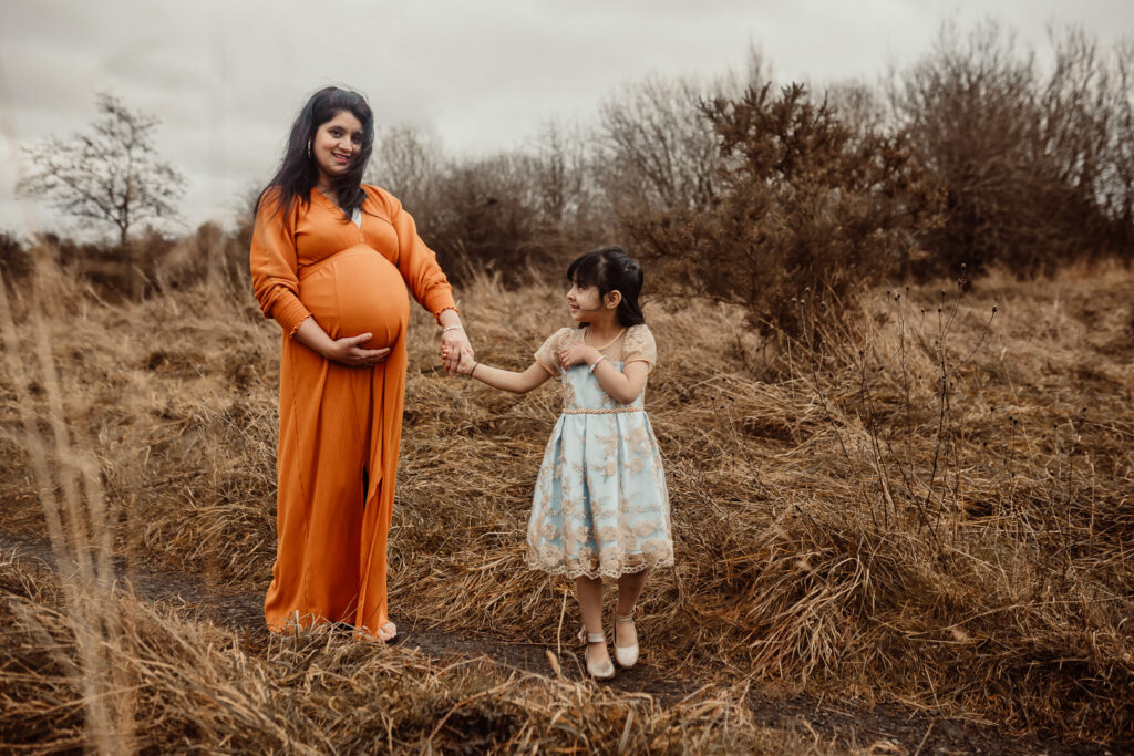 Mother and daughter walking through a meadow during a family photo session in Glasgow. Outdoor family photography capturing their bond in a natural and timeless way.