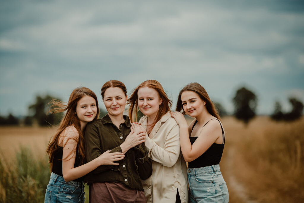 Mother with her three daughters during an outdoor family photoshoot in Scotland. Natural family photography capturing genuine connection, laughter and beautiful family moments in a meadow.