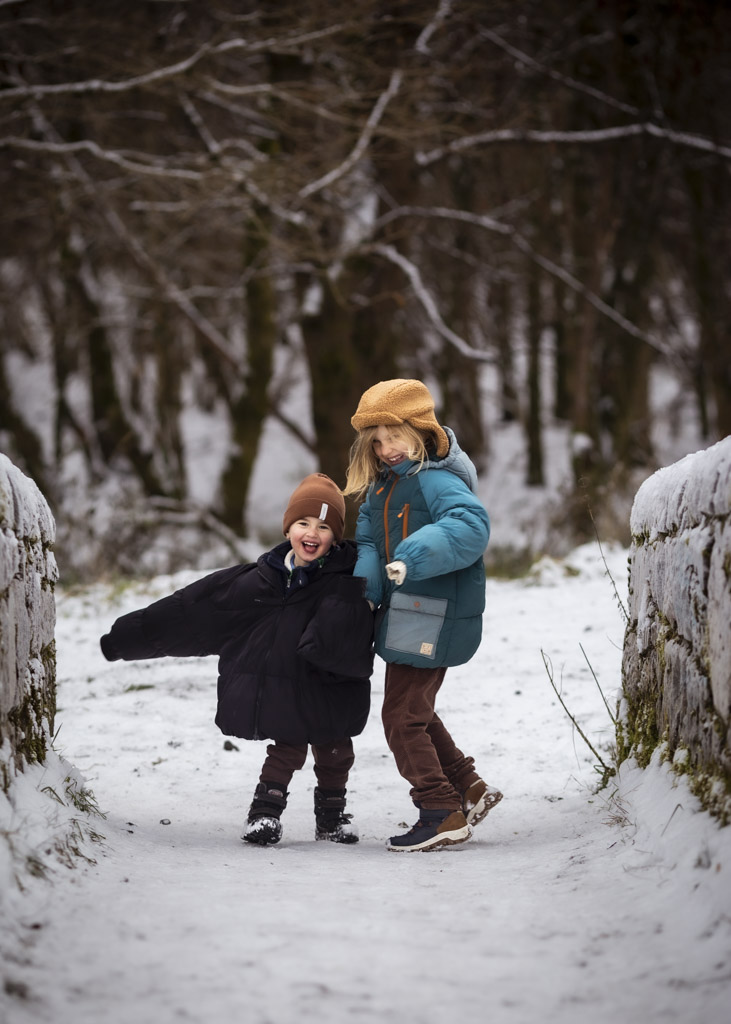 Two children laughing together in the snow during a winter family photoshoot in Glasgow