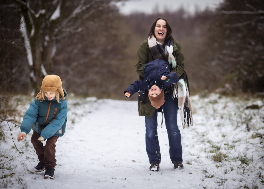 Mother laughing as she plays with her two children in the snow during a winter family photoshoot in Glasgow