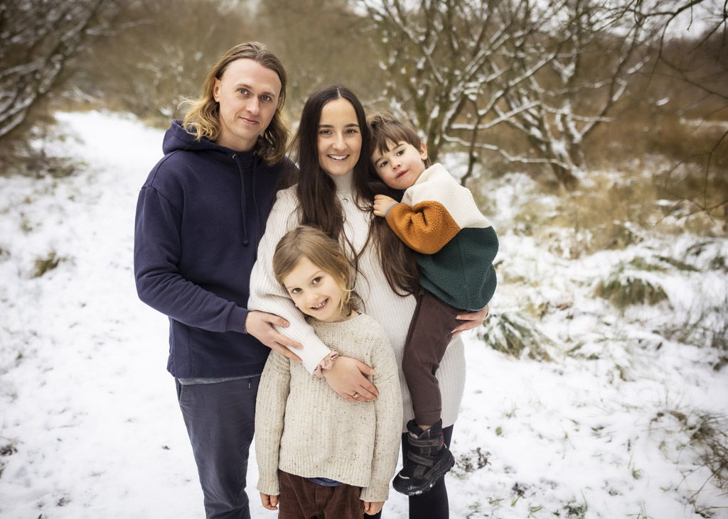 Family of four posing together in a snowy woodland during a winter family photoshoot in Glasgow