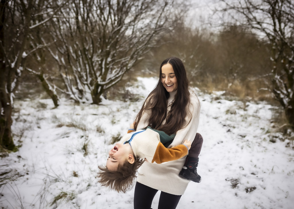 sister playfully walking with her younger brother through the snow during a winter family photoshoot in Glasgow