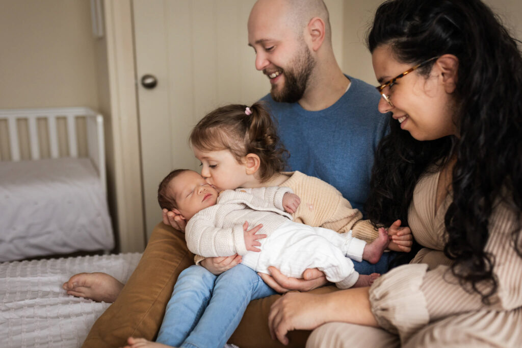 Family with a newborn and young daughter posing on a bed during a newborn photoshoot at home in Glasgow