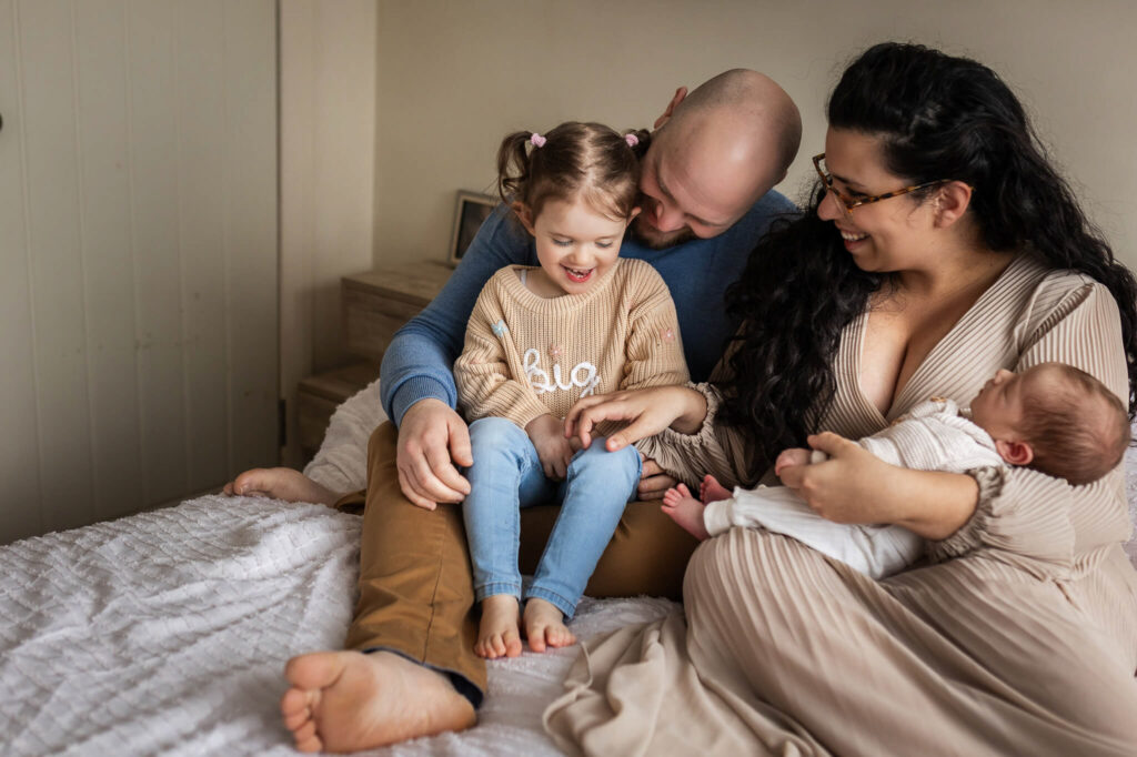 Family of four laughing and playing together during relaxed newborn photography session at home