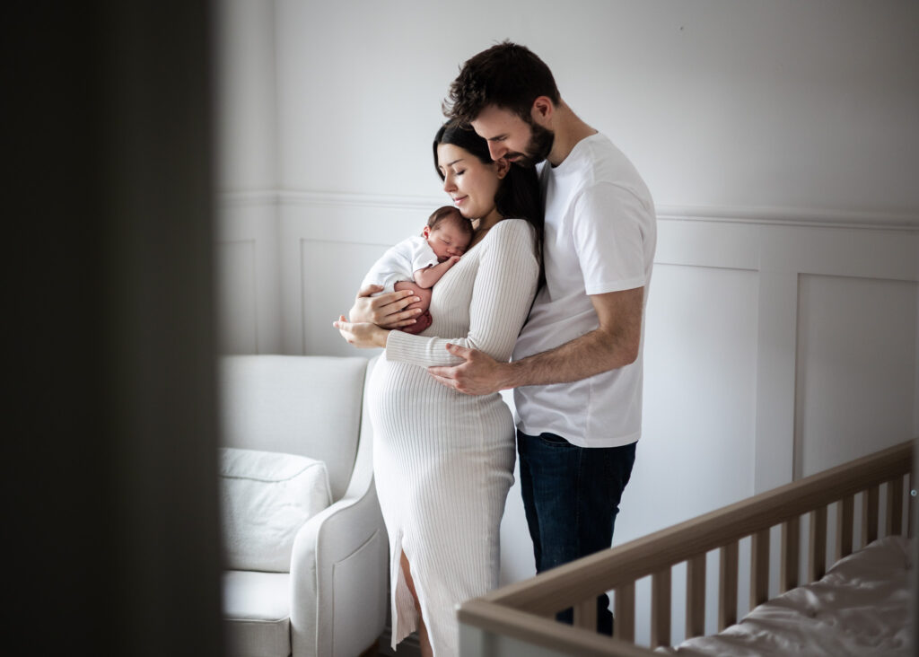 parents holding their newborn baby by the window at home